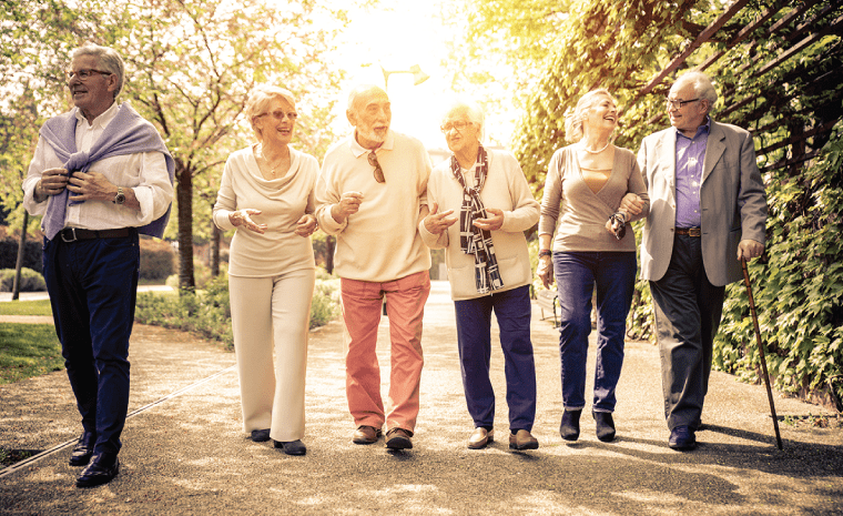 Group of senior citizens walking down a road smiling and talking to one another