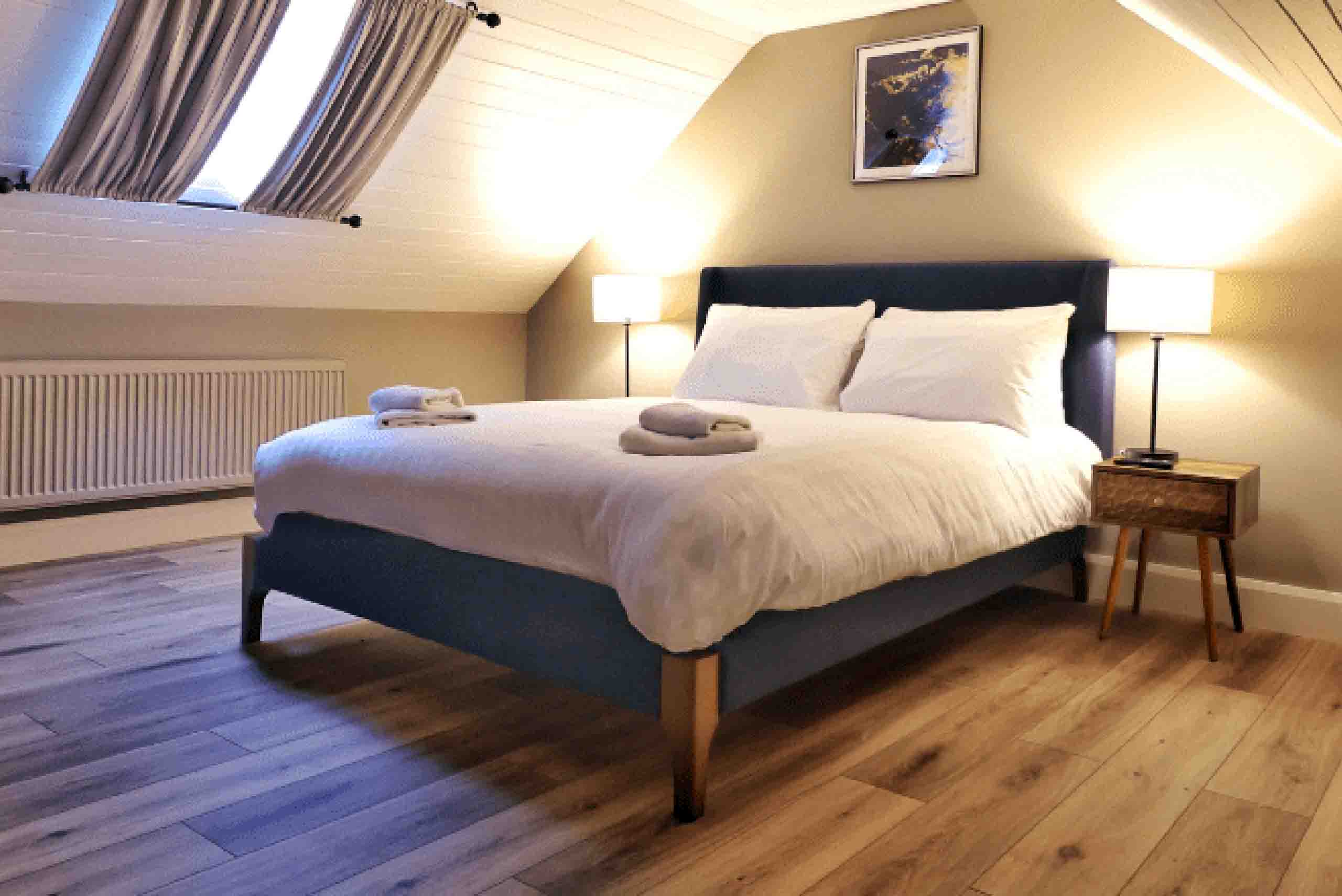 Self-Catering Cottages at Wells - Gamekeepers Bedroom 1 Double bed with white linen in soft lighting with dormer windows in the Gamekeeper Cottage at Wells