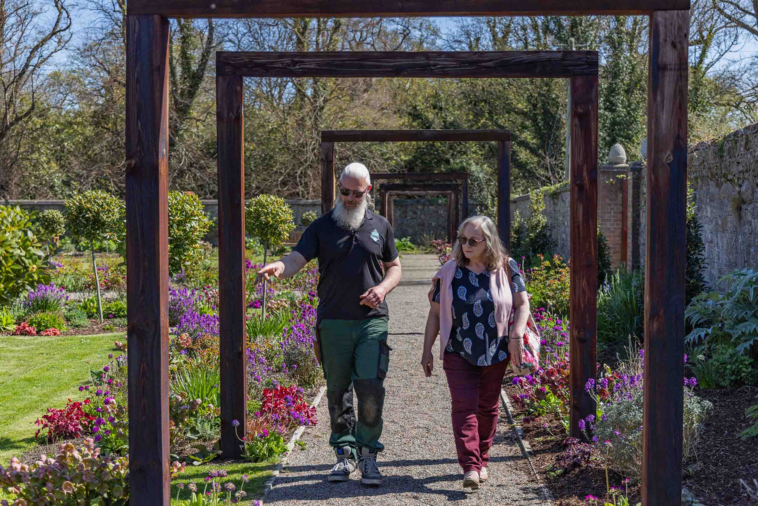 Head Gardener at Wells walking alongside a lady on his right explaining the planting in the Walled Garden during a Garden Tour