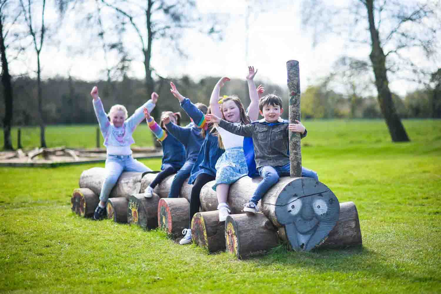 A group of Children waving from wooden carved train in the play area at Wells House